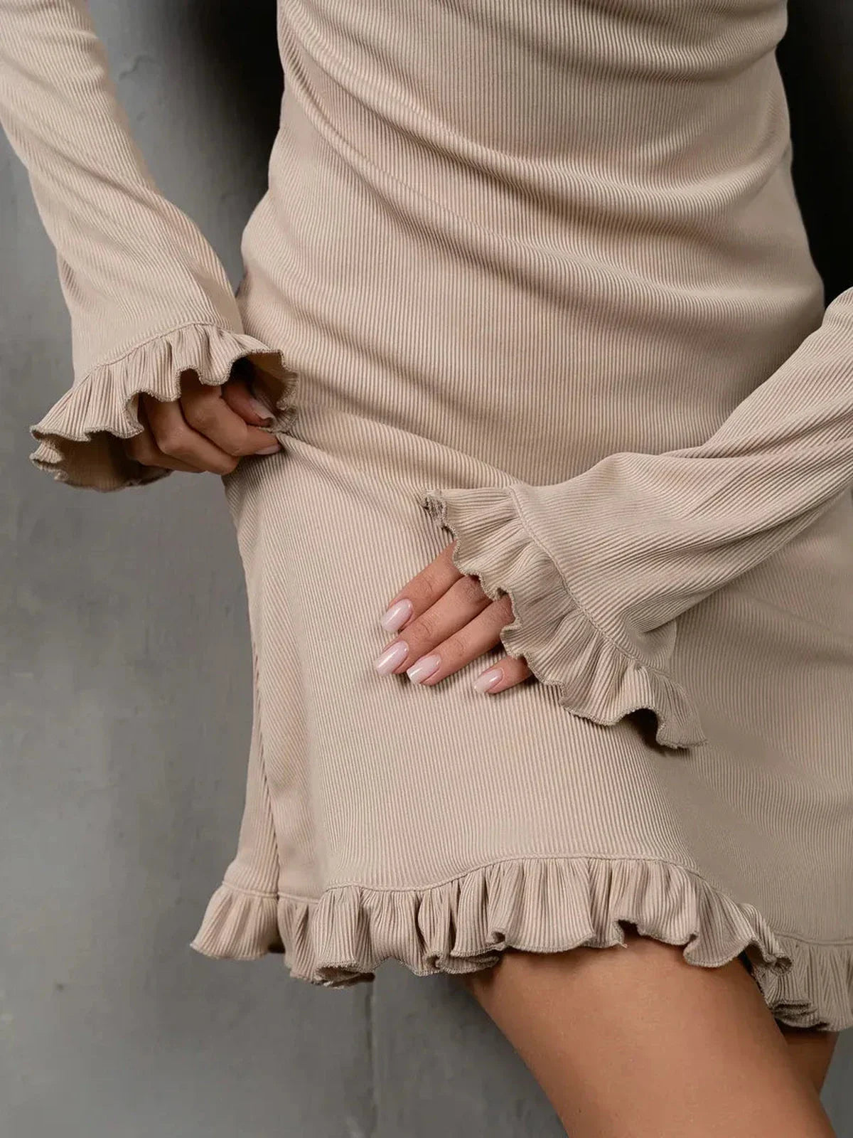 Close-up of a beige long sleeve dress featuring ruffle accents and a ribbed texture, embodying modern elegance.