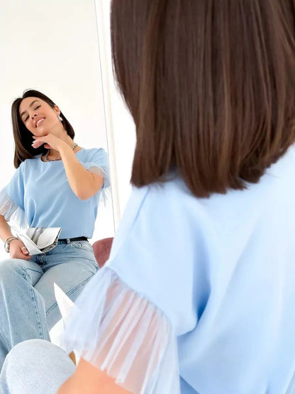 Celeste Blouse by Lauven, light blue silky top with tulle details, showcased in elegant reflection.