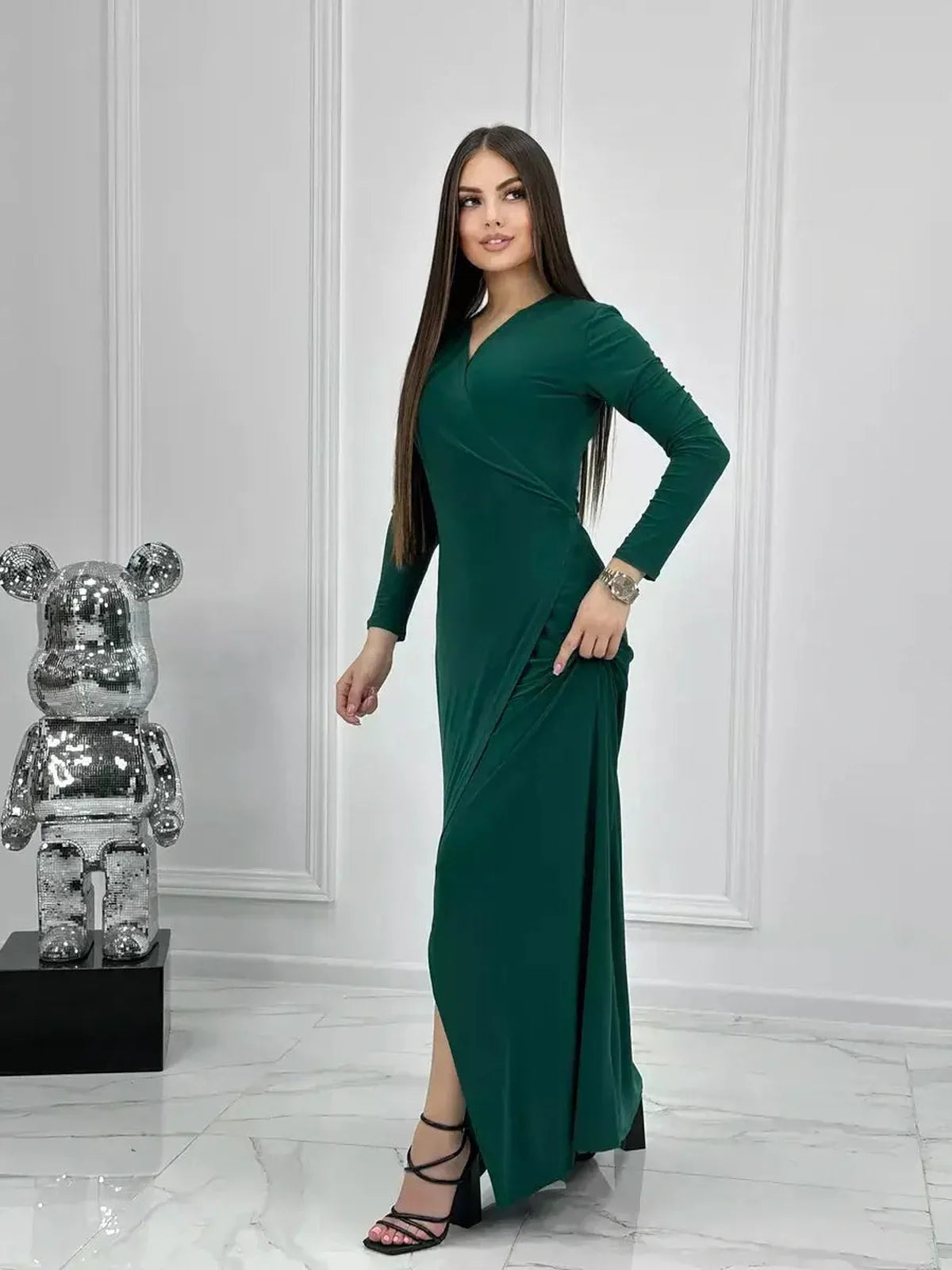 Woman modeling an elegant Emerald Allure Maxi Dress with a wrap silhouette and side slit, complementing a contemporary setting.