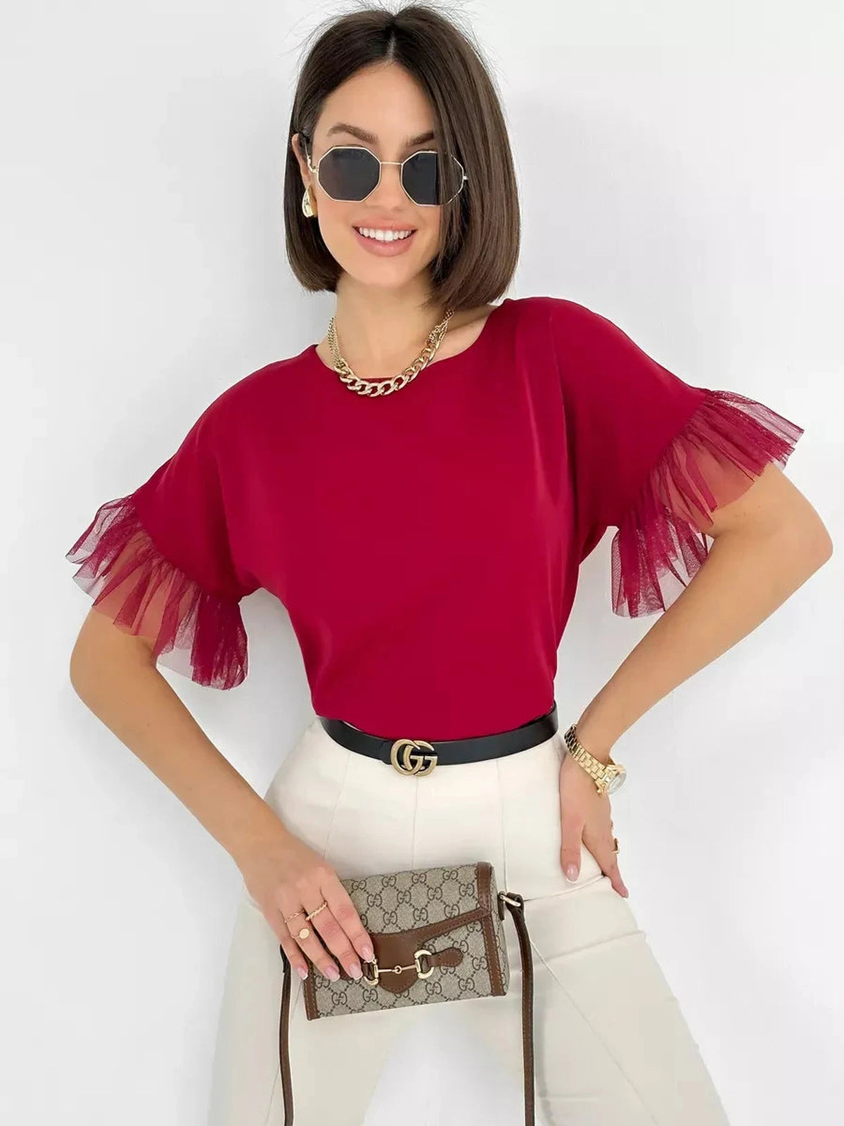 Model wearing Velora Blouse in burgundy with sheer ruffle sleeves, styled with sunglasses and handbag.