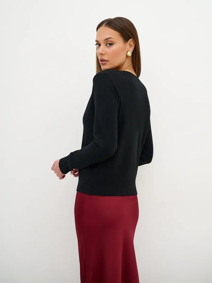 Model showcasing the Orion Cardigan in black, paired with a burgundy dress, highlighting its sleek design and versatile style.