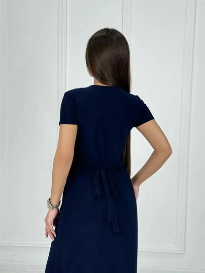 Back view of a woman in a navy Eclipse Maxi Dress with a sleek wrap bodice and tied waist.
