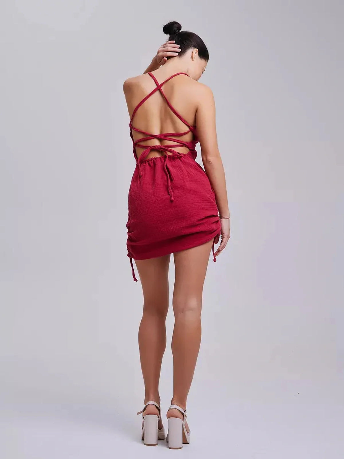 Model showcasing the back of a fitted crimson mini dress with intricate lace-up detail.