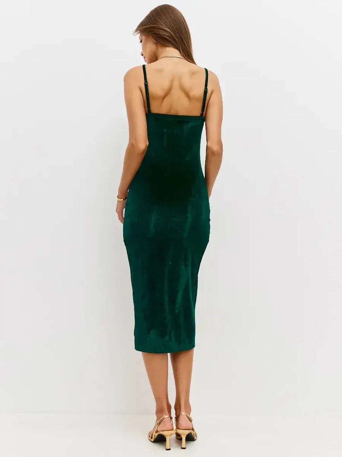 Back view of a model in a luxurious emerald velvet midi dress with fine straps and a body-hugging silhouette.