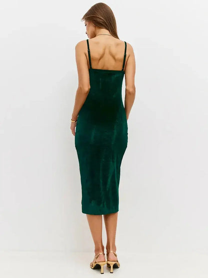 Back view of a model in a luxurious emerald velvet midi dress with fine straps and a body-hugging silhouette.