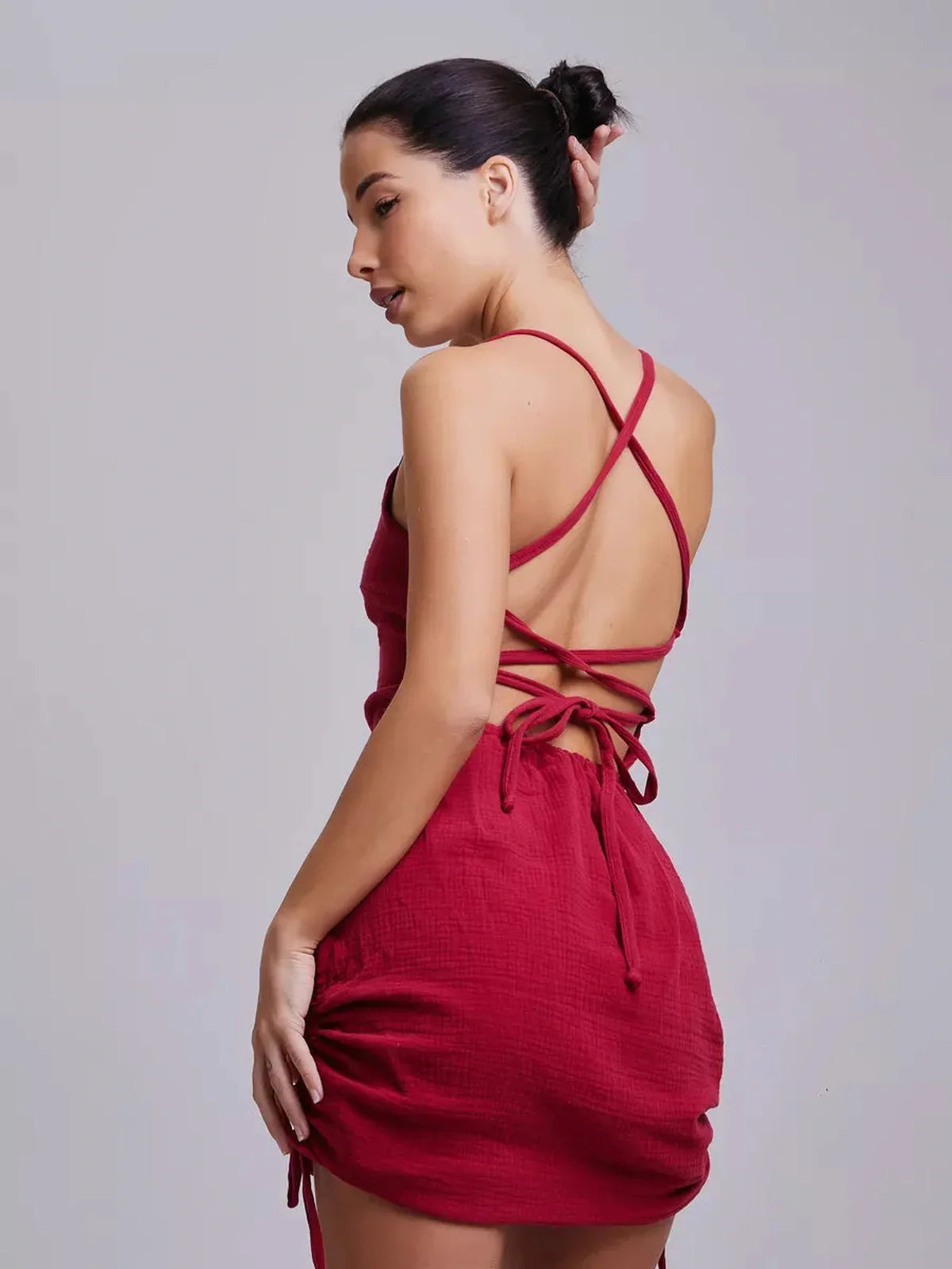 Model showcasing the back of a fitted crimson mini dress with lace-up detail, perfect for summer occasions.