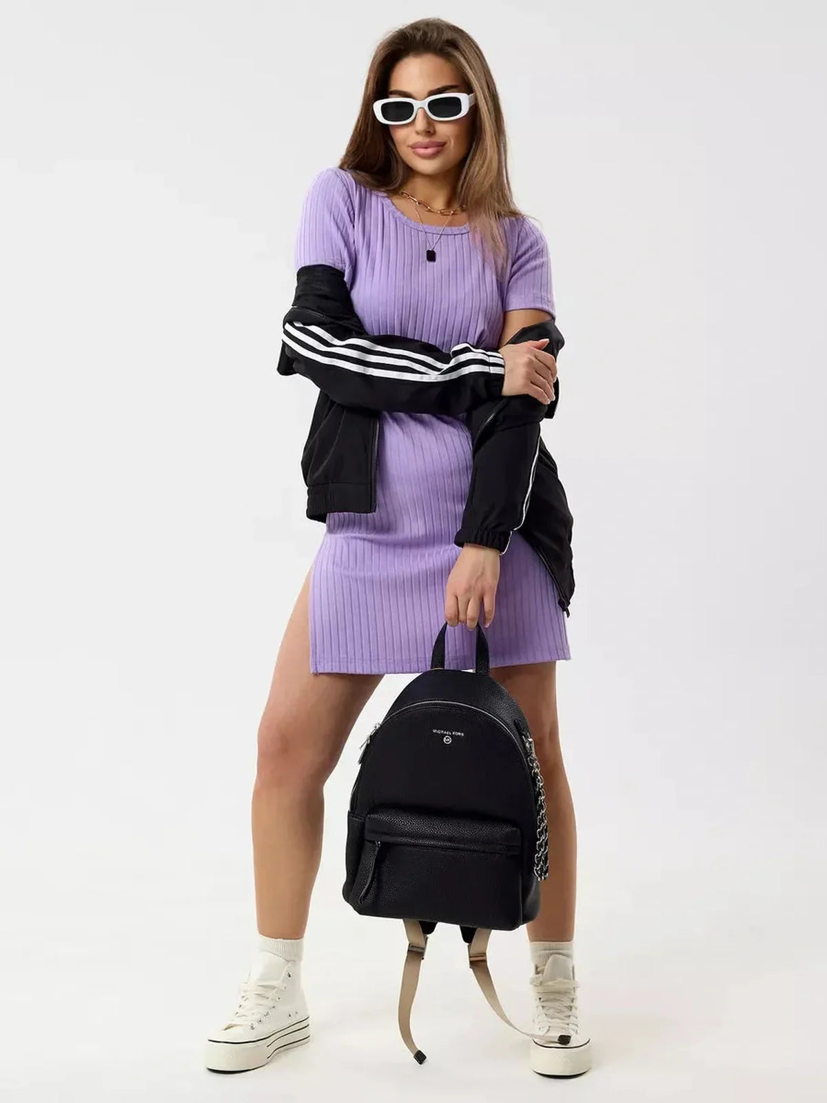 Model showcasing the Lilac Ripple mini dress in violet, featuring ribbed texture, short sleeves, and minimalist design, styled with a backpack.