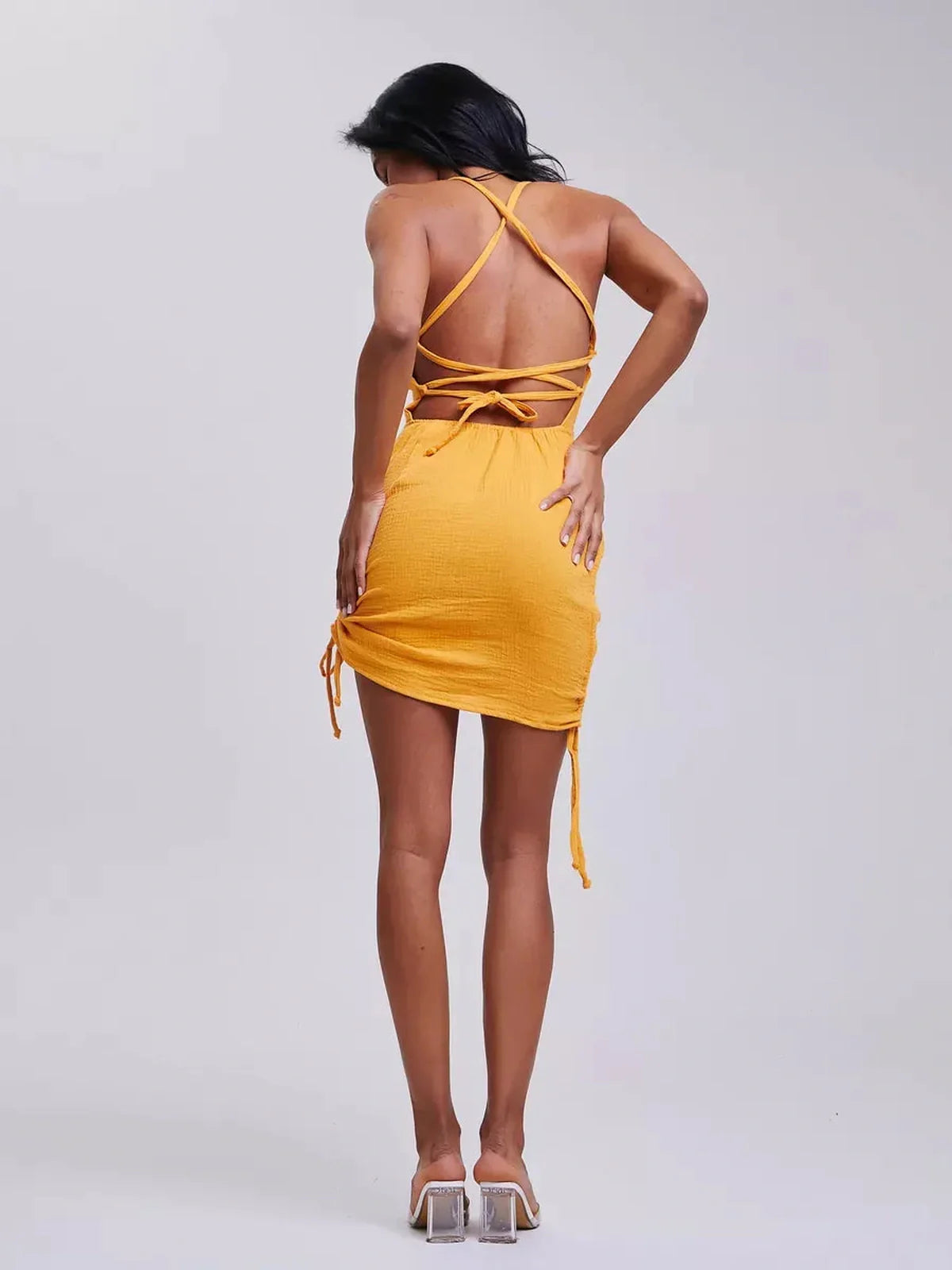Back view of a woman in a yellow bodycon mini dress with adjustable crisscross straps for summer styling.