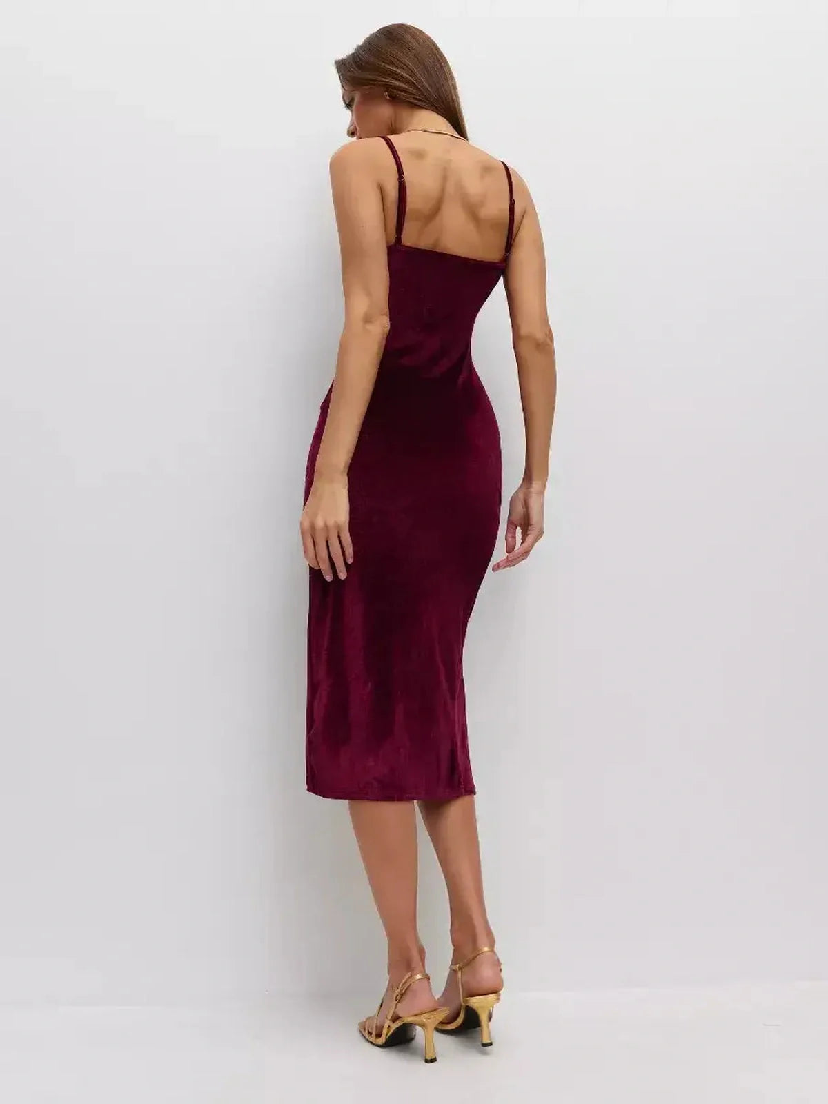 Back view of a woman in a burgundy midi dress made of plush velvet, featuring thin straps and an elegant silhouette.