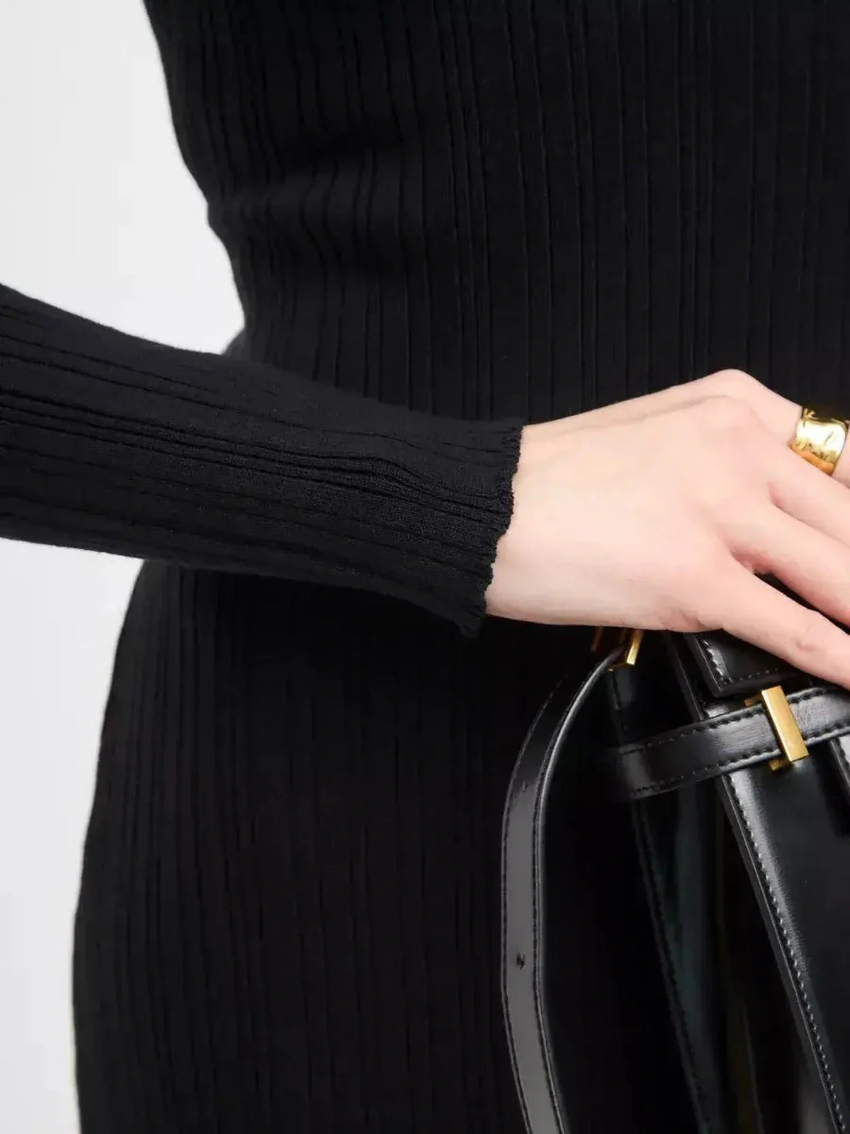 Close-up of a woman's hand holding a black handbag, showcasing the ribbed texture of a black maxi dress.