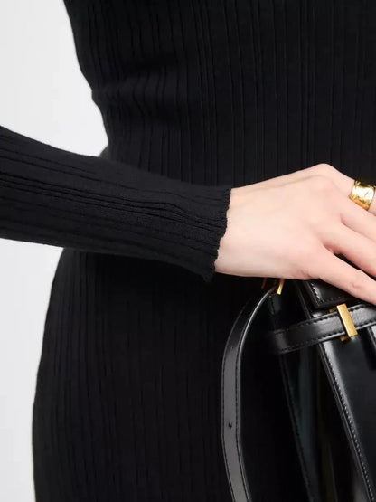 Close-up of a woman's hand holding a black handbag, showcasing the ribbed texture of a black maxi dress.