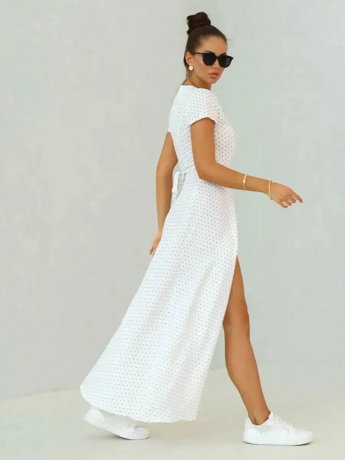 Model wearing an ivory dots maxi dress with wrap silhouette and high slit, paired with sneakers for a casual summer look.
