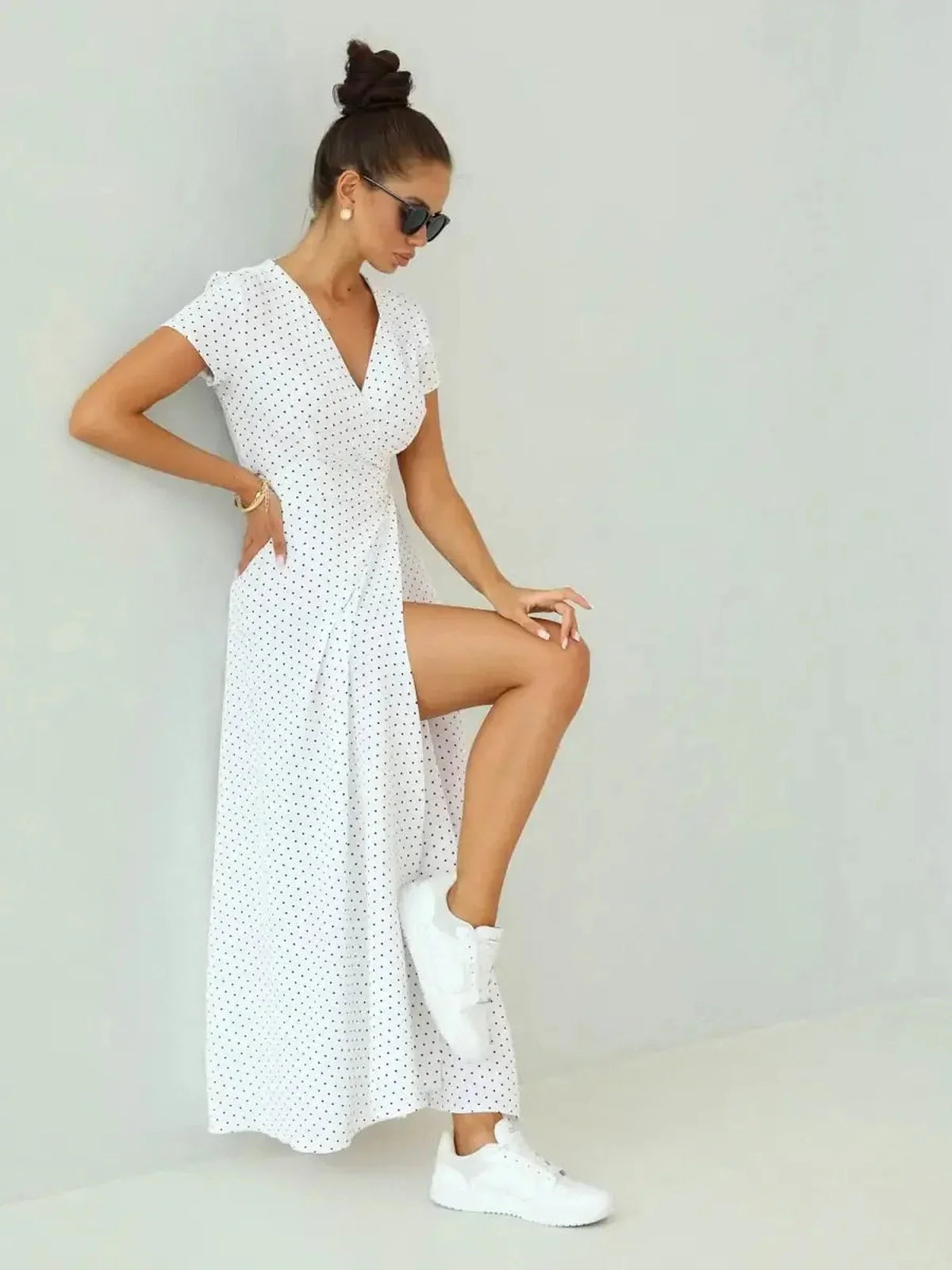 Woman in ivory dots maxi dress with wrap silhouette, stylishly paired with white sneakers against a neutral backdrop.