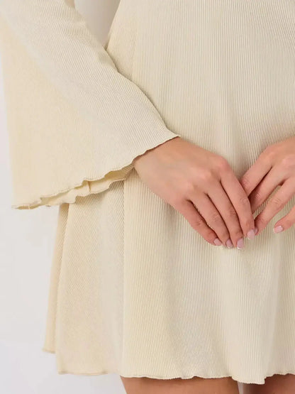 Close-up of hands holding the hem of the Ivory Flare mini dress by Lauven, showcasing ribbed texture and flared sleeves.