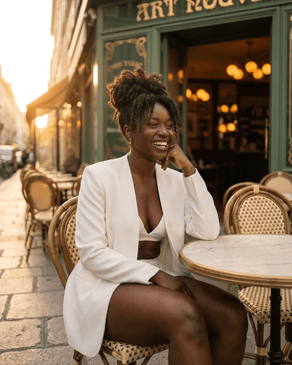 Woman wearing Alba Blazer by Lauven, smiling at a café table in a chic outdoor setting.