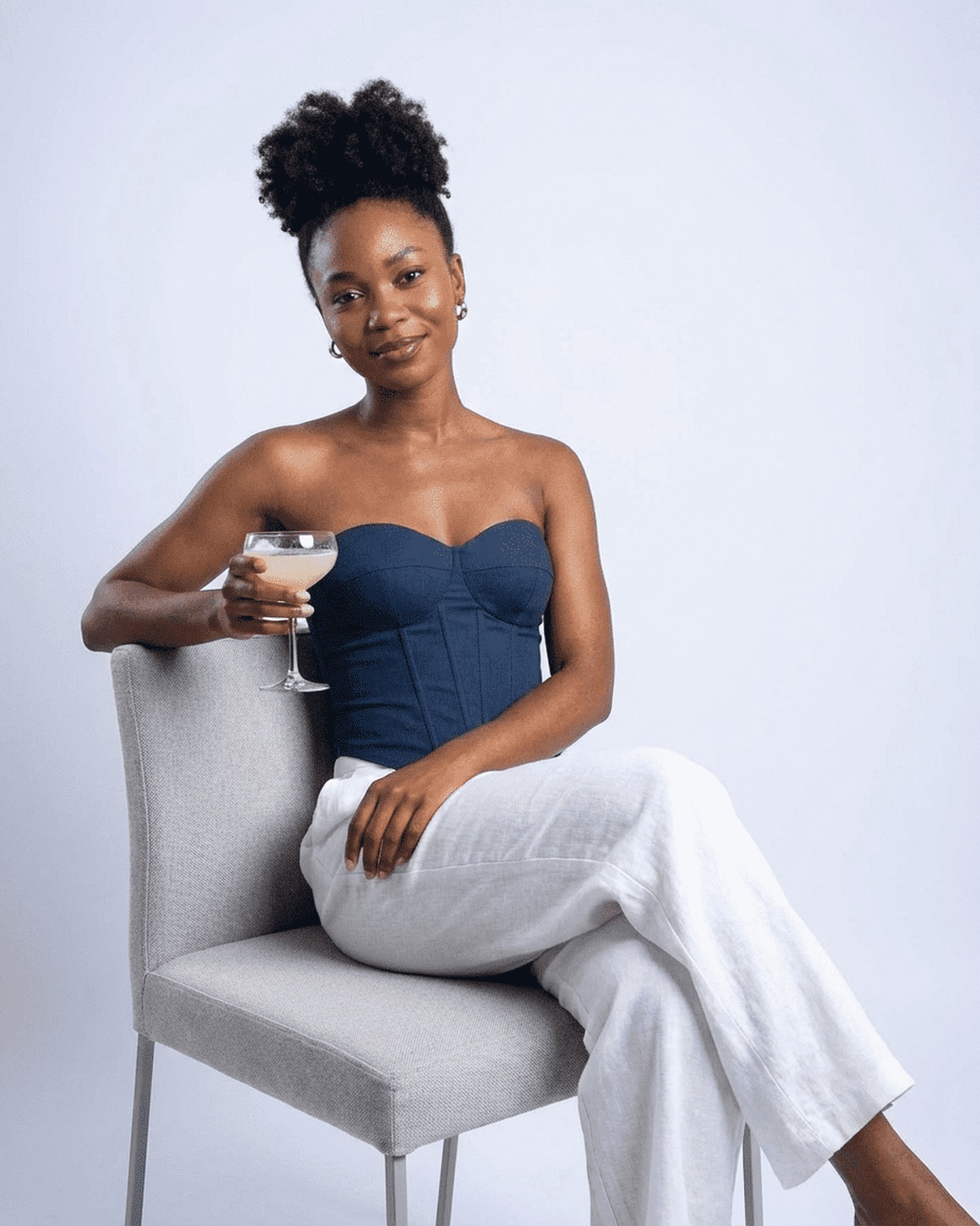 Model wearing the Atlas Corset Top by Lauven, navy faux denim bustier, holding a cocktail, seated elegantly.