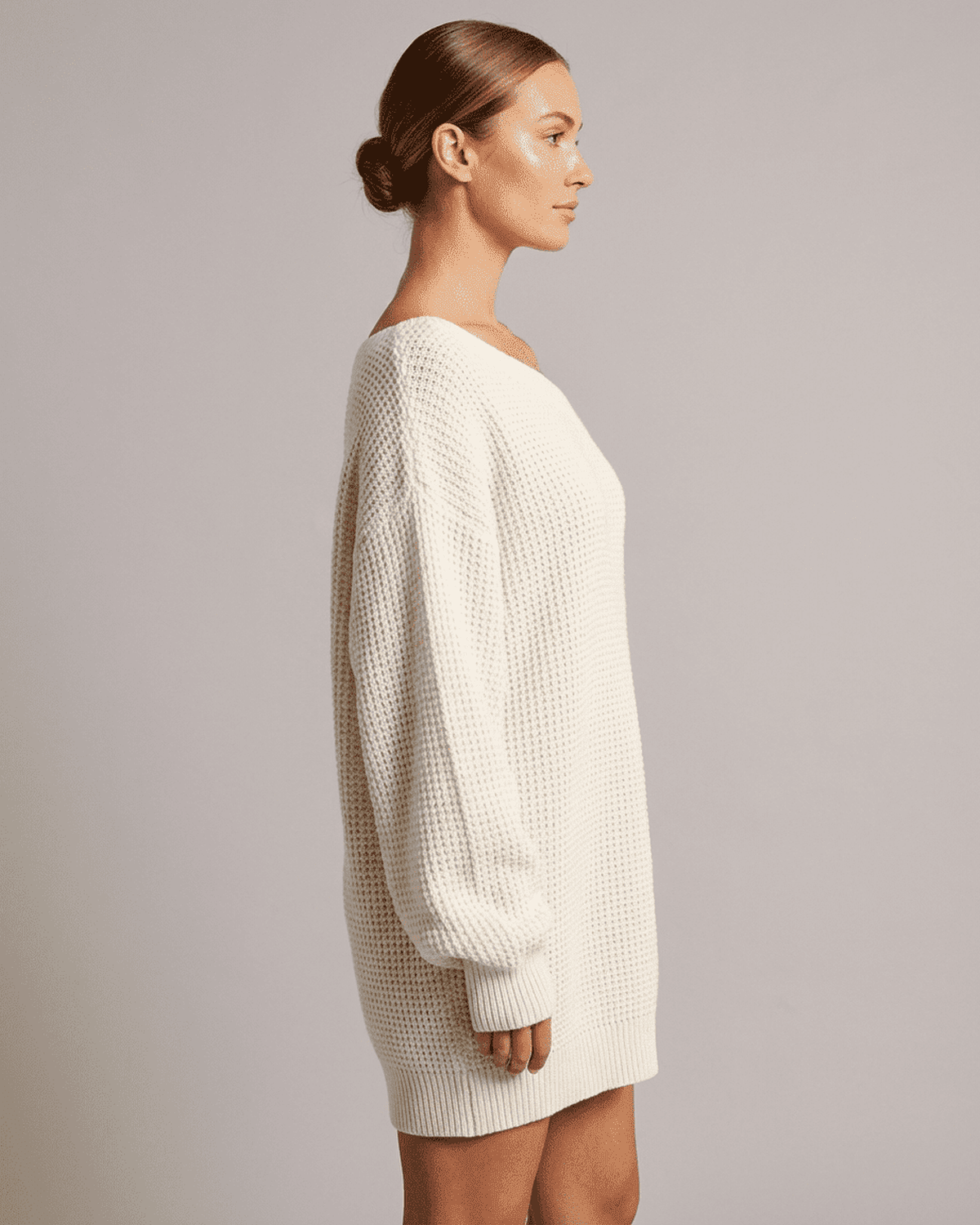 Side view of a woman wearing the Lauven Aurora Mini Dress, featuring a cozy white ribbed knit design.
