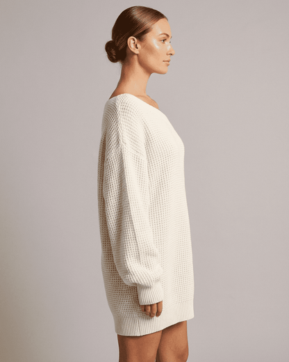 Side view of a woman wearing the Lauven Aurora Mini Dress, featuring a cozy white ribbed knit design.