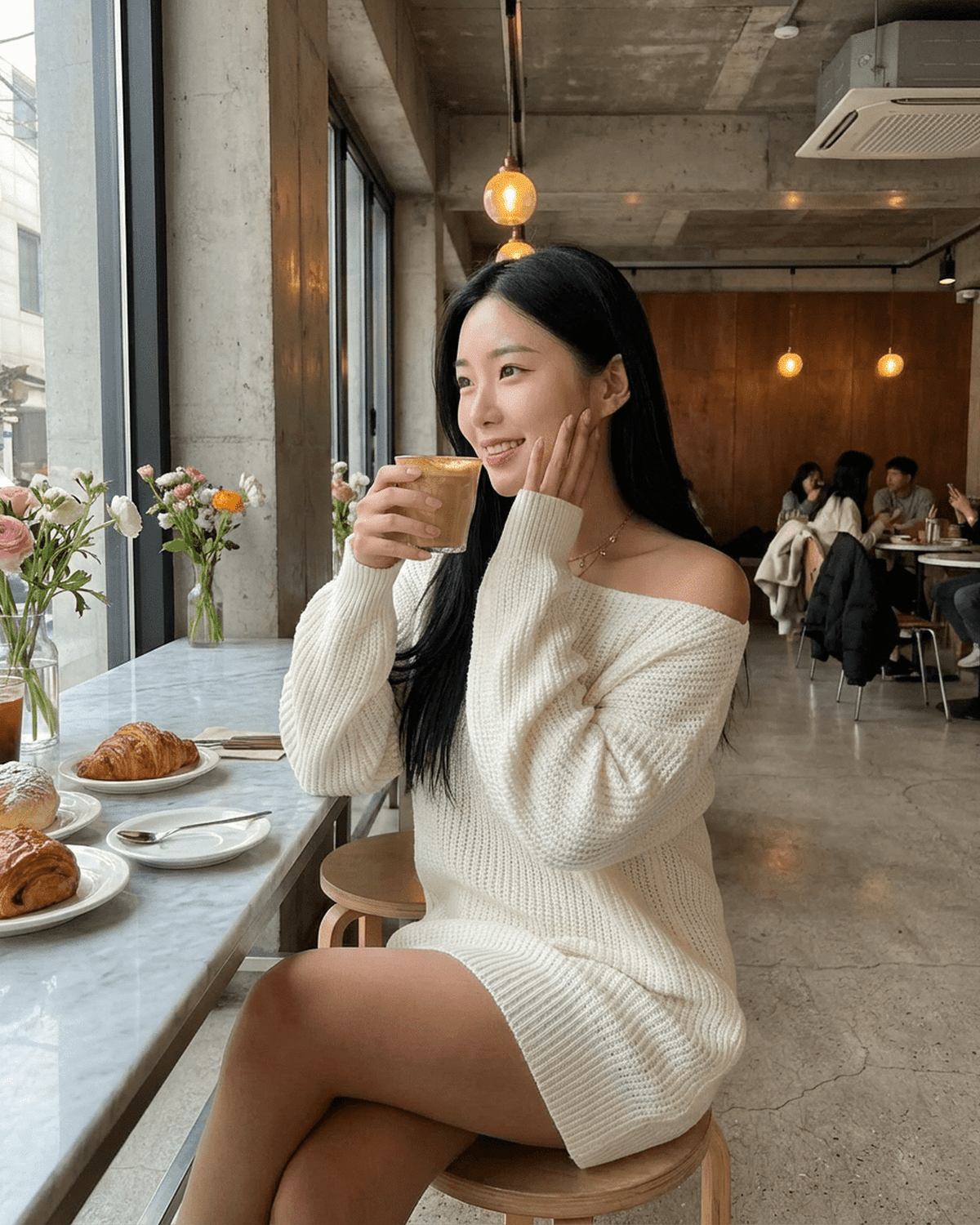 Woman enjoying a beverage in a cafe wearing the Aurora Mini Dress by Lauven, featuring an off-the-shoulder design.