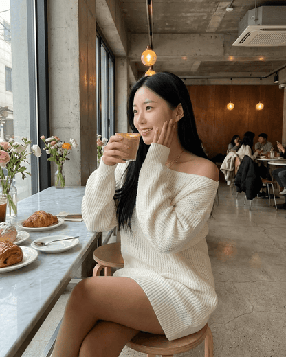 Woman enjoying a beverage in a cafe wearing the Aurora Mini Dress by Lauven, featuring an off-the-shoulder design.