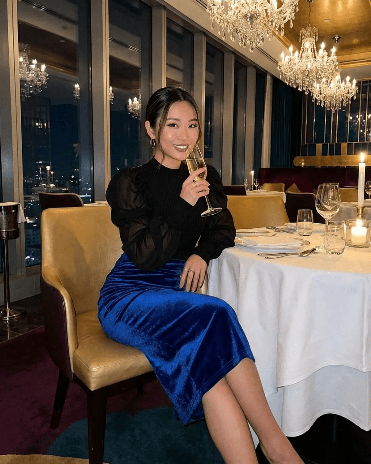 Woman wearing Azure Midi Skirt by Lauven, enjoying a drink at an elegant restaurant setting.