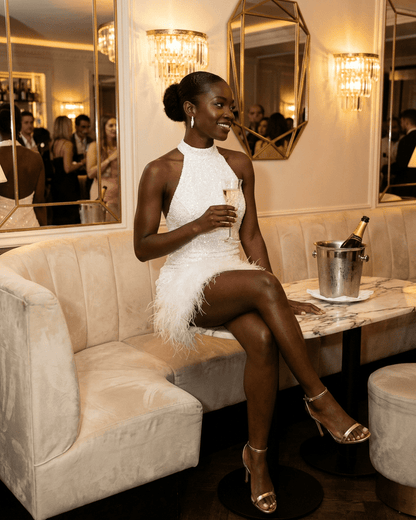 Bianca Mini Dress by Lauven, showcasing a white sequin halter bodycon design with a fuzzy hem at an elegant venue.