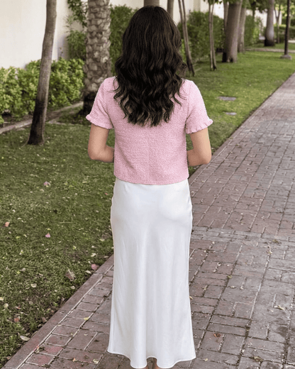 Back view of woman in Camellia Cardigan by Lauven, styled with a white skirt in a garden setting.