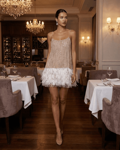 Celeste Mini Dress by Lauven, a sequin tulle fairycore mini dress with feather tassel hem in an elegant restaurant setting.
