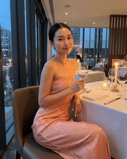 Model wearing Champagne Maxi Dress by Lauven, sitting elegantly at a dining table, holding a glass of wine.