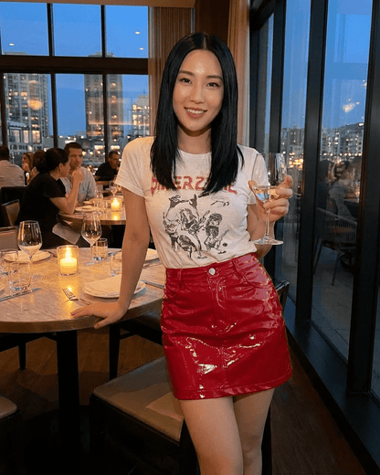 Woman in a restaurant wearing a Crimson Mini Skirt by Lauven, holding a drink, with city skyline in the background.