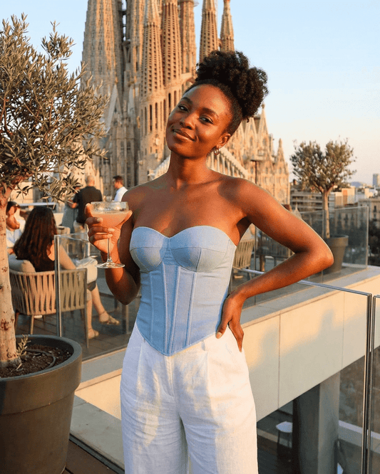 Denali Corset Top by Lauven, a faux denim cup bustier worn by a woman enjoying a cocktail with a city view.