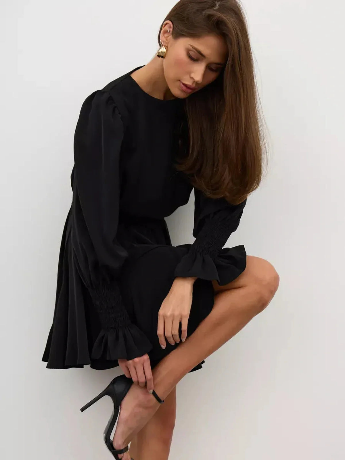 Model wearing Lauven Eclipse Mini Dress in black, featuring long sleeves and a ruffled hem, showcasing modern elegance.
