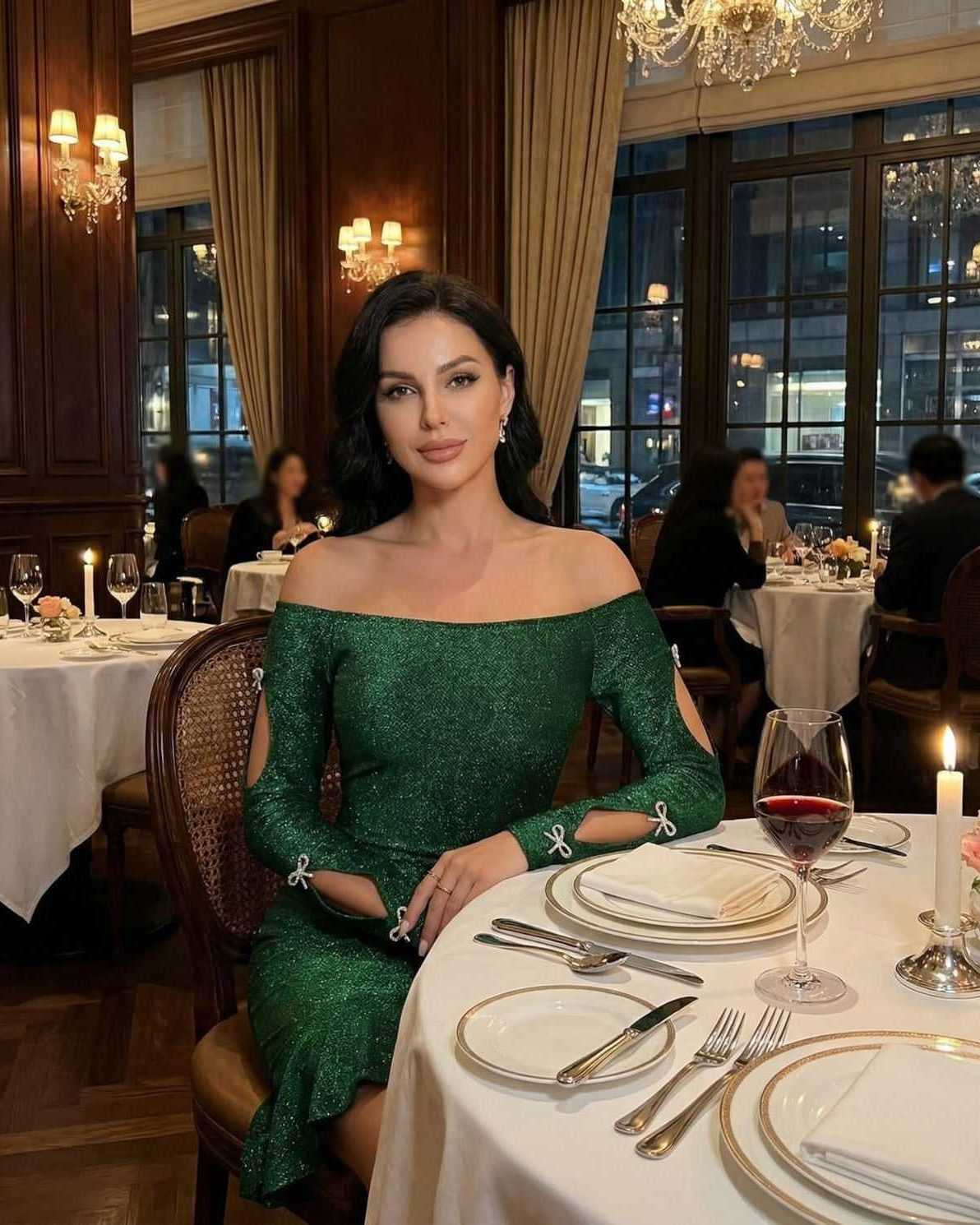 Elegant woman wearing an Emerald Mini Dress by Lauven, off-the-shoulder bodycon style with cutouts, sitting in a fine dining setting.