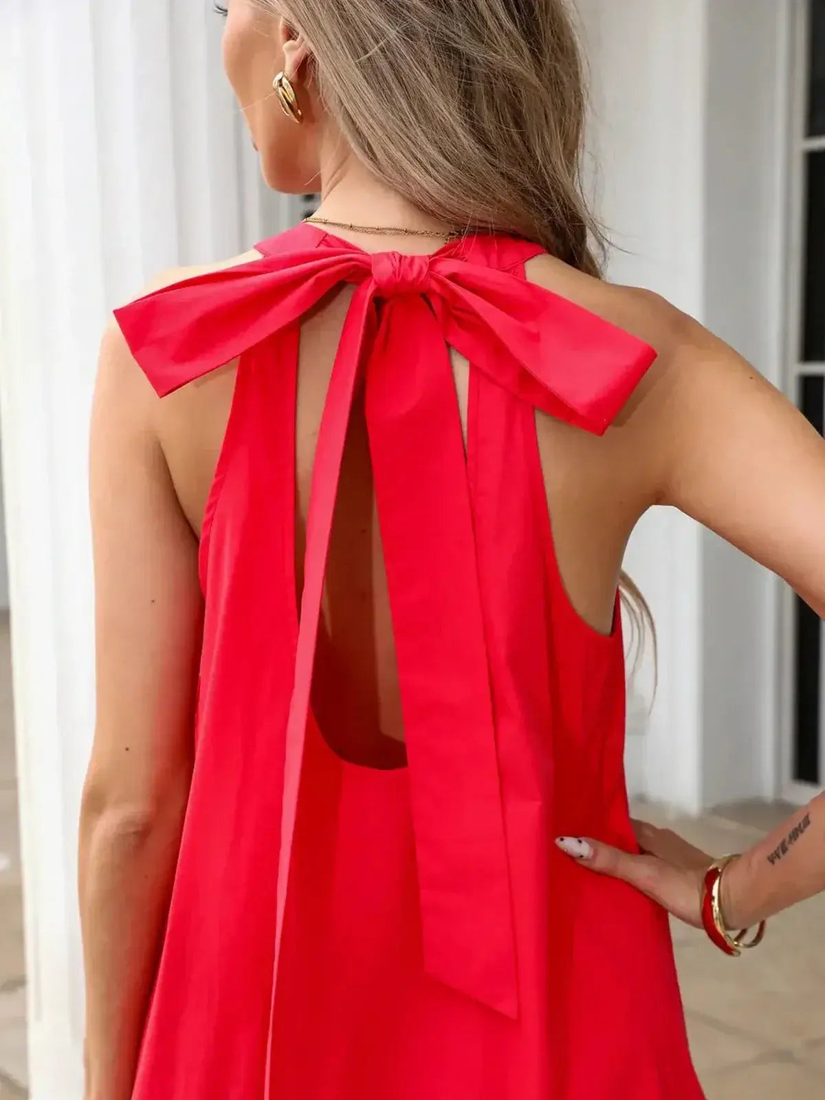 Back view of a woman wearing a vibrant fuchsia halter mini dress with a large bow tie and open back design.