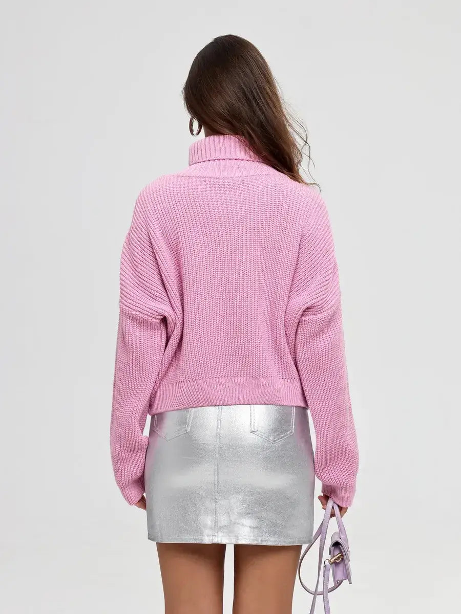 Back view of a woman wearing the Iris Sweater by Lauven, an oversized pink knit with a turtleneck, paired with a silver skirt.