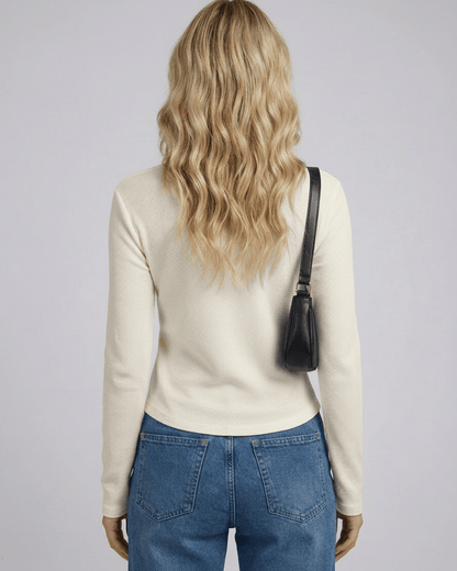 Back view of a woman wearing the Liora Long Sleeve Henley top in cream with denim jeans and a black handbag.