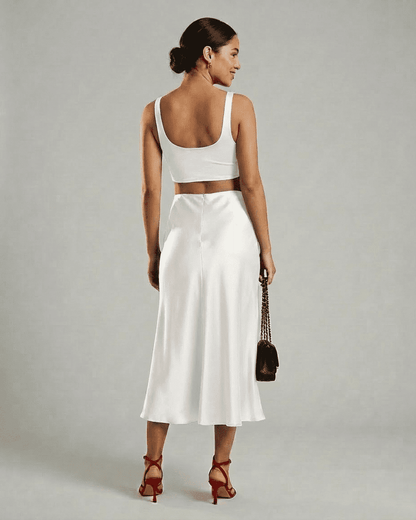 Woman in white back view wearing Lauven Luna Midi Skirt and cropped top, showcasing elegant satin mermaid design.