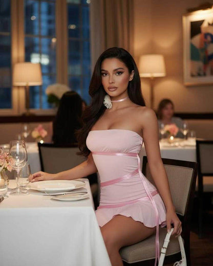 Luna Mini Dress by Lauven in light pink with satin ribbon detailing, showcasing a strapless design at an elegant dinner setting.