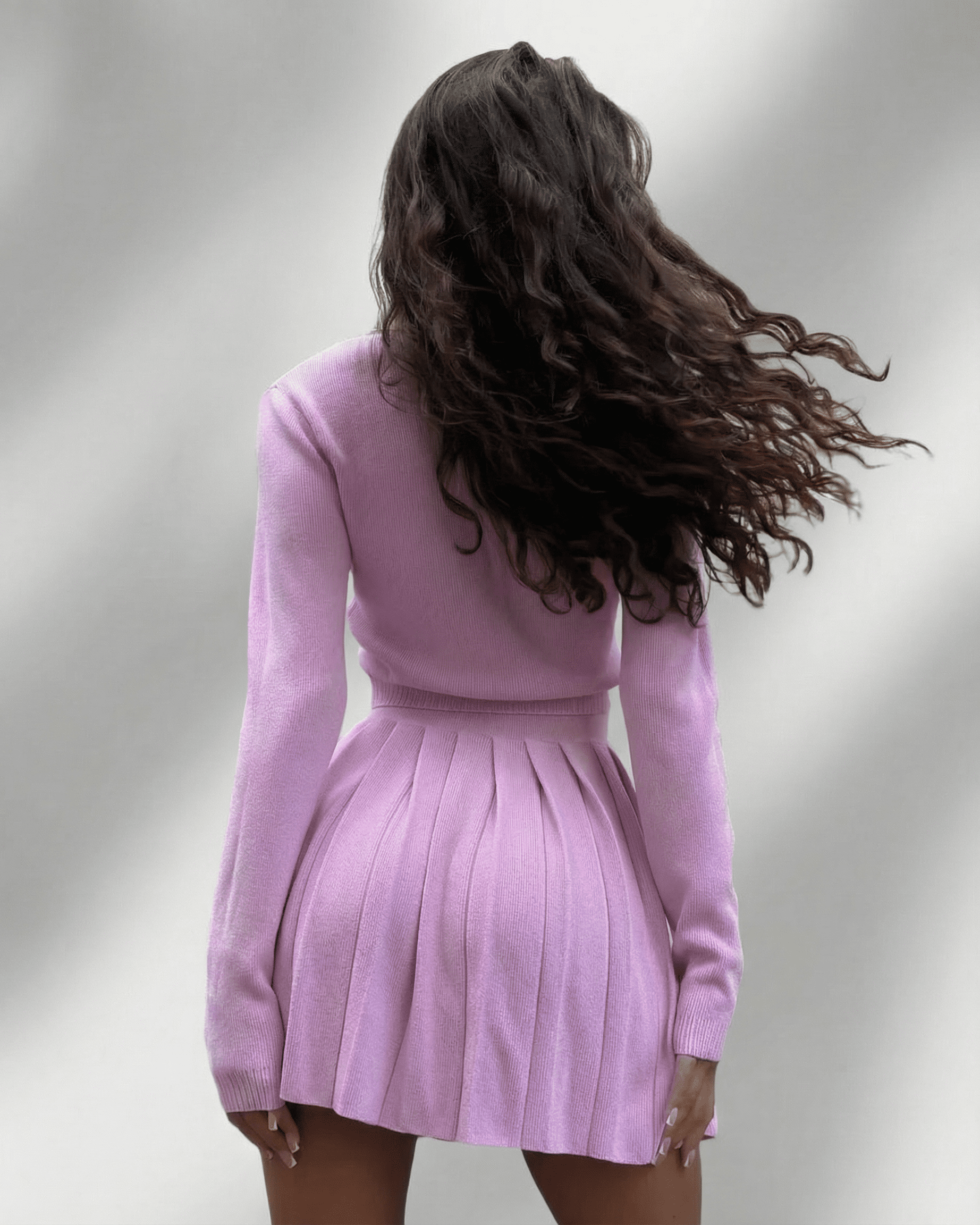 Back view of a model wearing the Lyra Two-Piece Set by Lauven featuring a soft knit cardigan and pleated mini skirt.