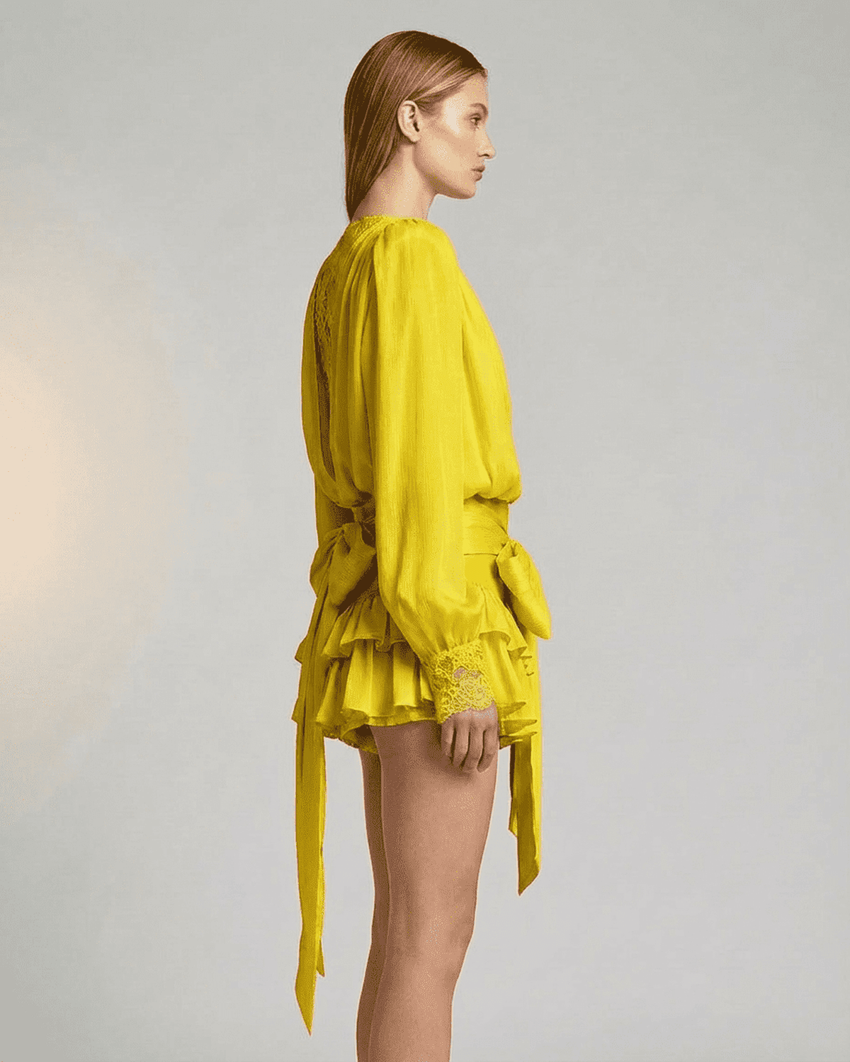 Side view of a model wearing the Lauven Marigold Mini Dress with lace detail, showcasing its V-neck and tiered silhouette.