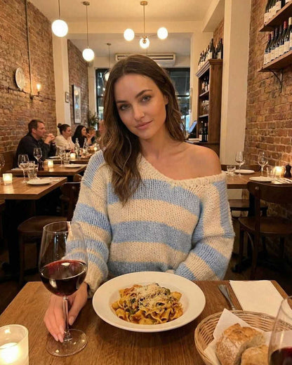 Woman wearing Marina Pullover by Lauven, enjoying dinner with pasta and red wine in a cozy restaurant.