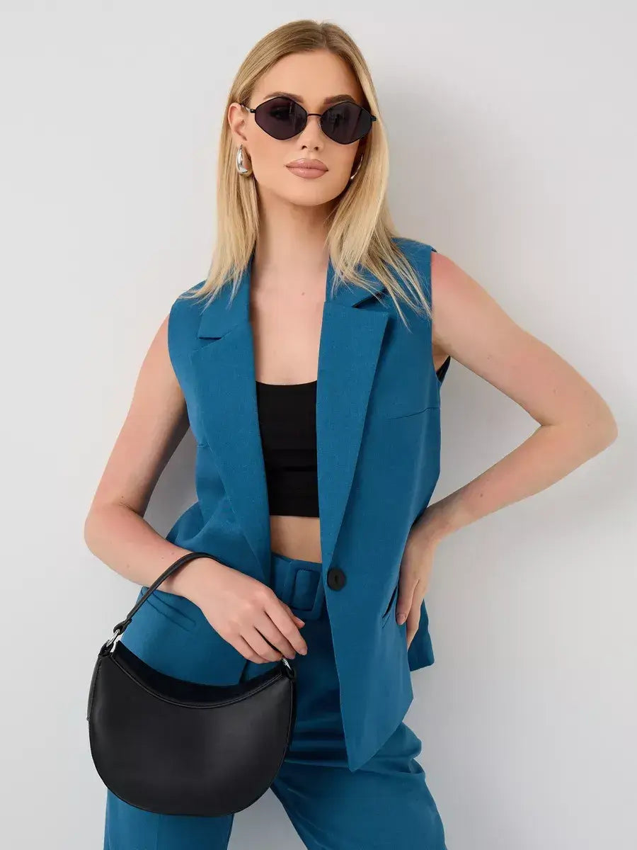 Model wearing Marine Suit Set by Lauven featuring sleeveless teal vest and high-waist pants, posing with a black handbag.