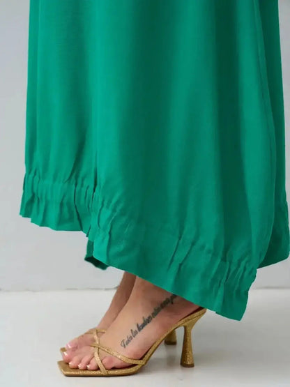 Close-up of a green maxi dress hem with ruffled detail, paired with golden heeled sandals.