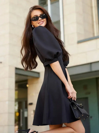Lauven Midnight Grace black mini dress with puff sleeves showcased outdoors, styled with sunglasses and a handbag.