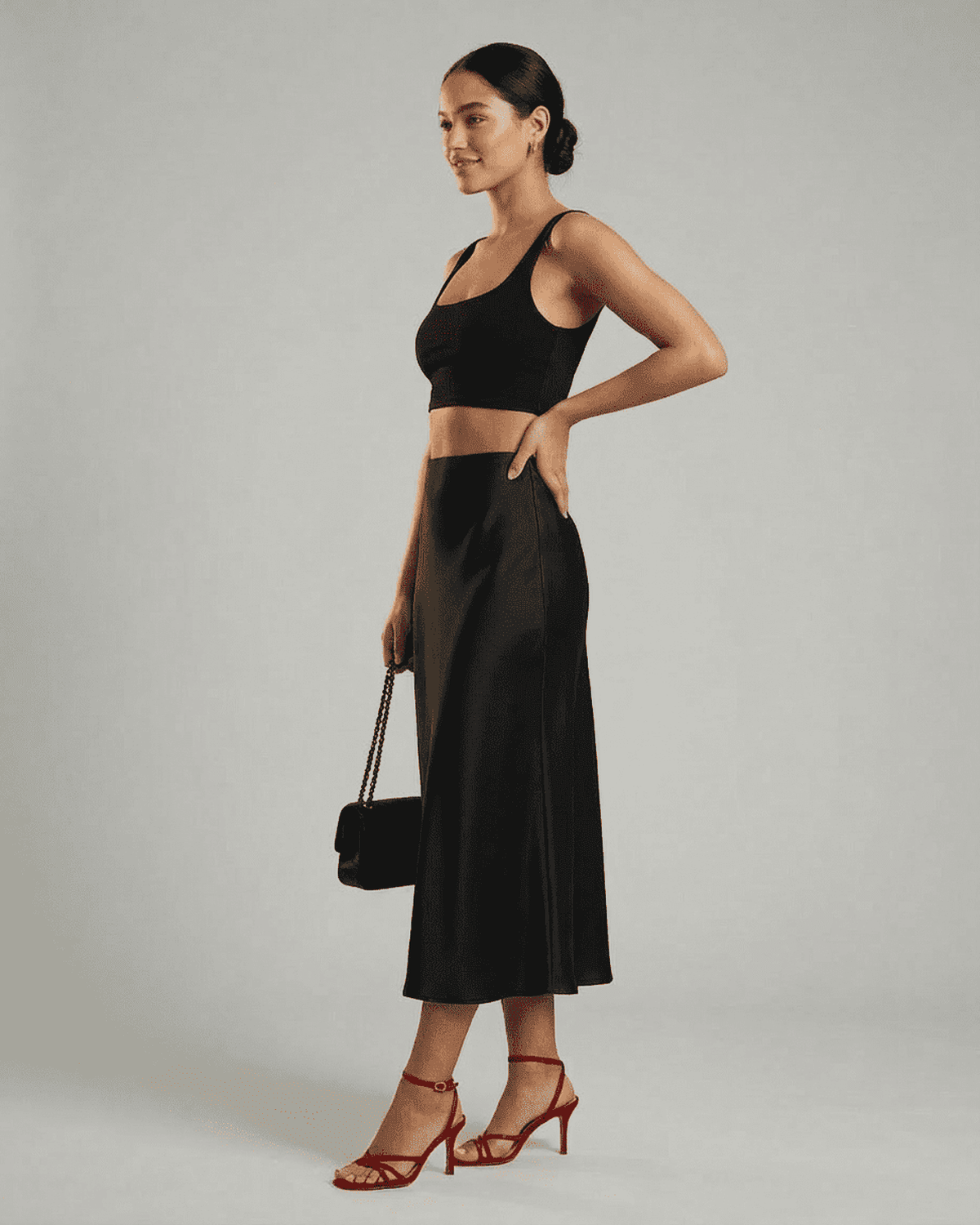 Model wearing Lauven Noirelle Midi Skirt, a sleek satin mermaid midi skirt, styled with a black top and red heels.
