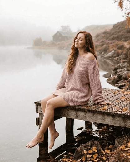 Nova Mini Dress by Lauven, showcasing a model in a soft pink ribbed knit off-the-shoulder design by a serene lake.