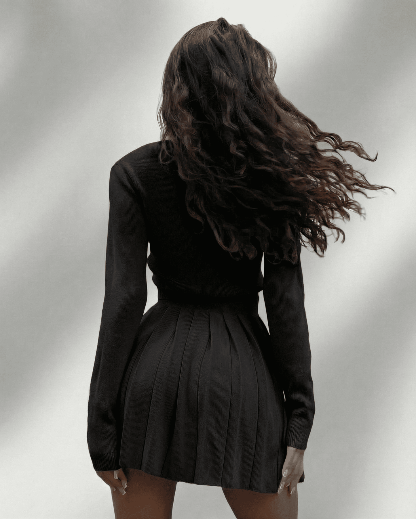 Nyx Two-Piece Set by Lauven featuring a model wearing a knit cardigan and pleated mini skirt from the back.