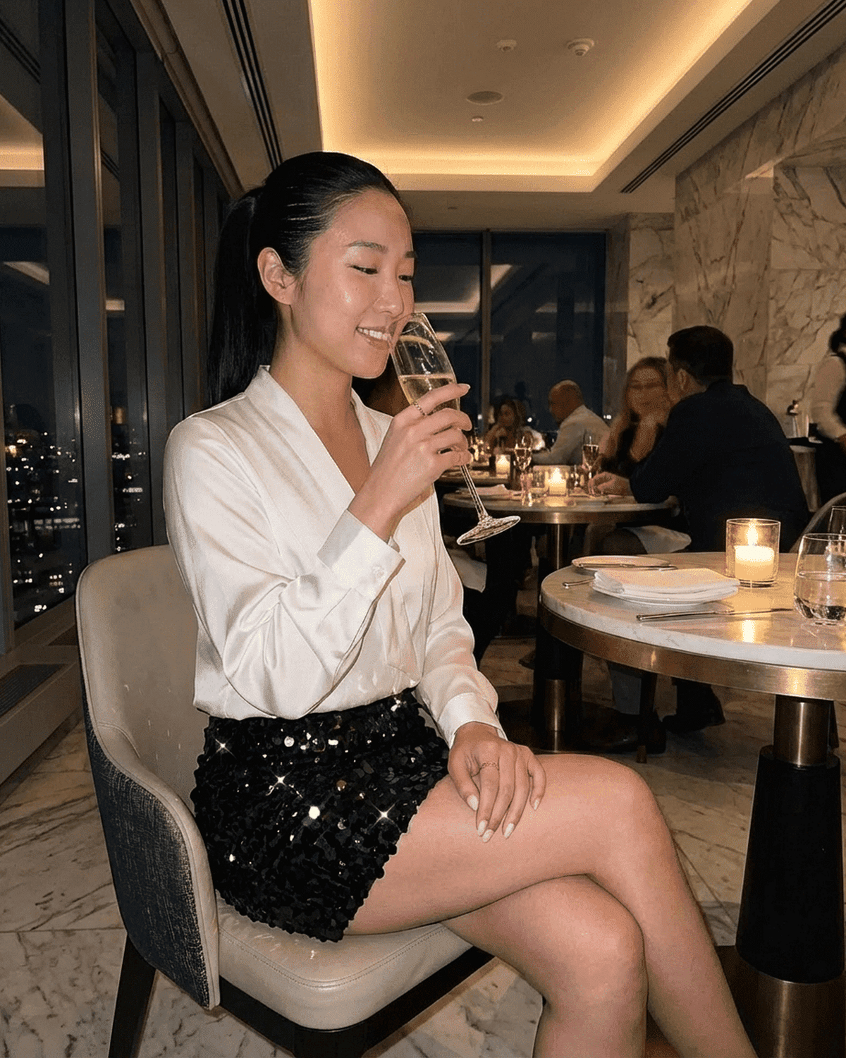 Stylish woman wearing Obsidia Mini Skirt by Lauven, enjoying a drink at an elegant evening setting.