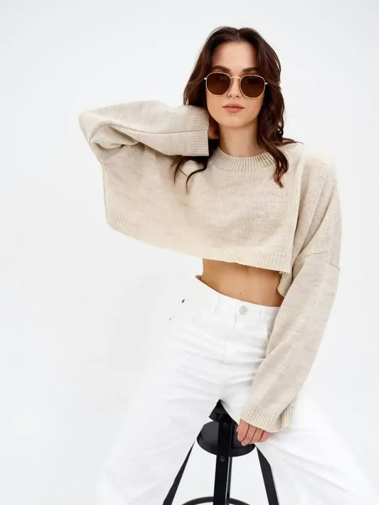 Model wearing a Sand Sweater by Lauven, a cropped oversized knit in light beige, styled with white jeans.