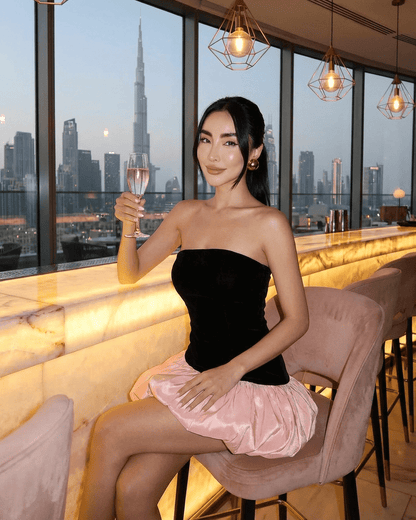 Selina Mini Dress by Lauven, featuring a strapless black velvet top and a playful pink puff skirt, against a city skyline.